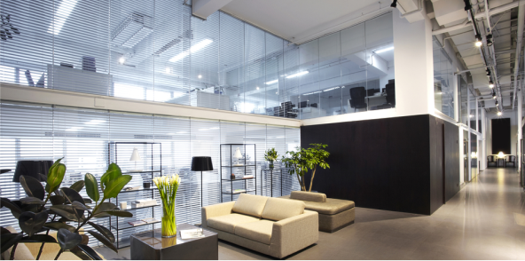 A industrial office featuring a large glass wall, abundant greenery, and a bright, inviting atmosphere filled with plants.